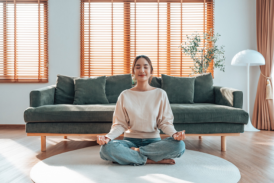 woman sits on floor in her home eyes closed legs crossed meditating in Beaverton